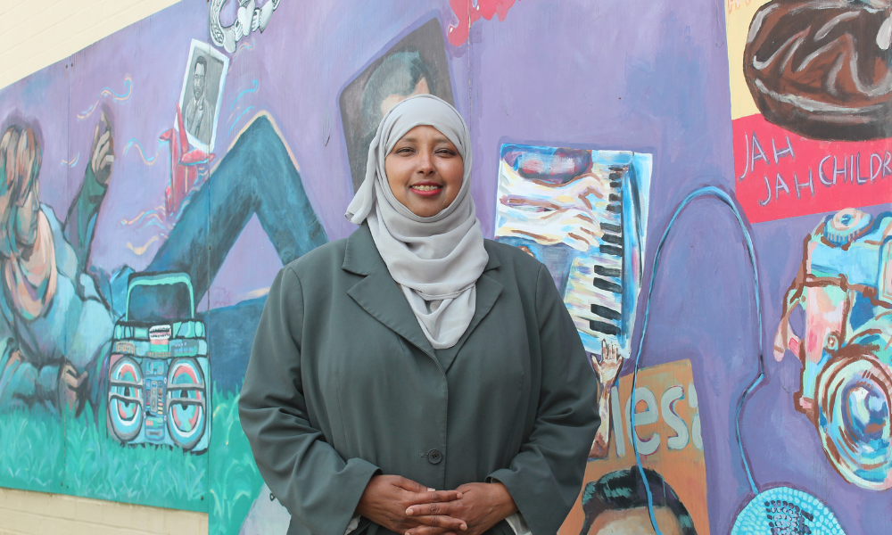 A woman smiling standing in front of a mural.