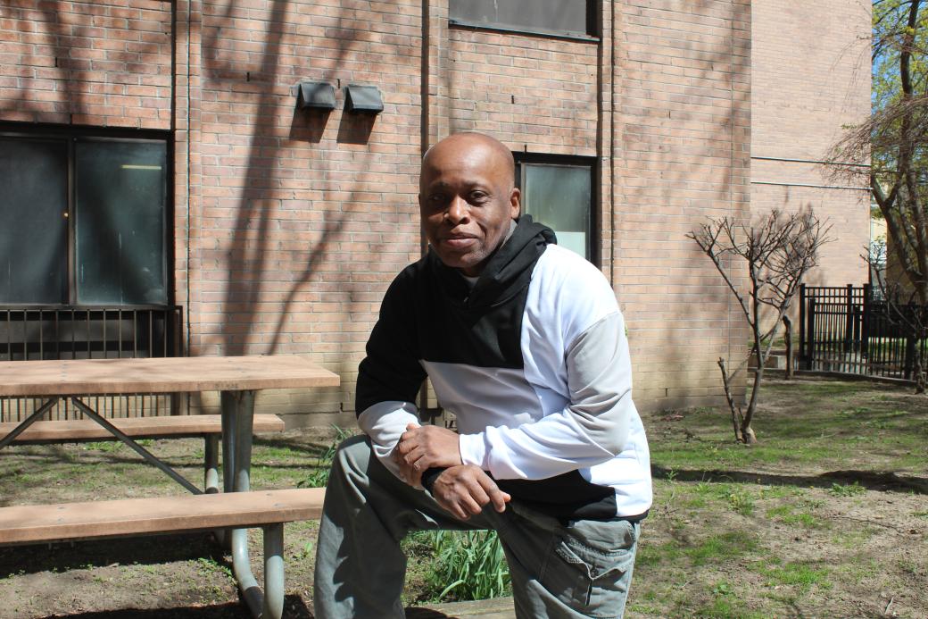 A photo of a man posing by a bench outdoors. 