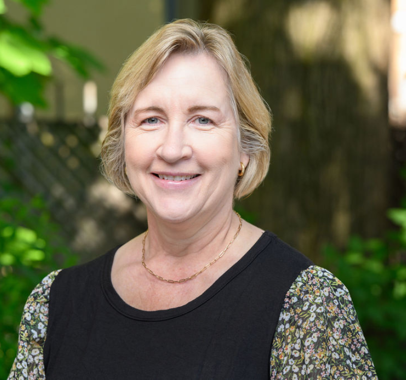A woman smiling with greenery in the background.