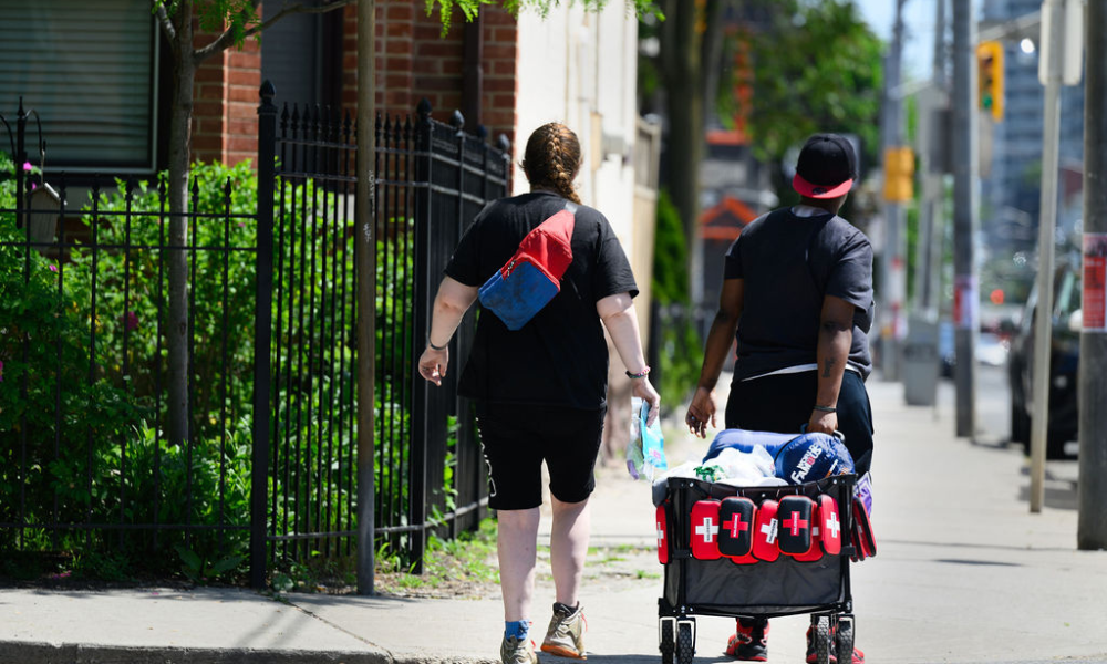 Two people walking down a street in Toronto pulling a cart of medical supplies.