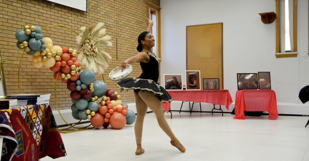 A Black woman wearing a ballet costume performing in a community room.