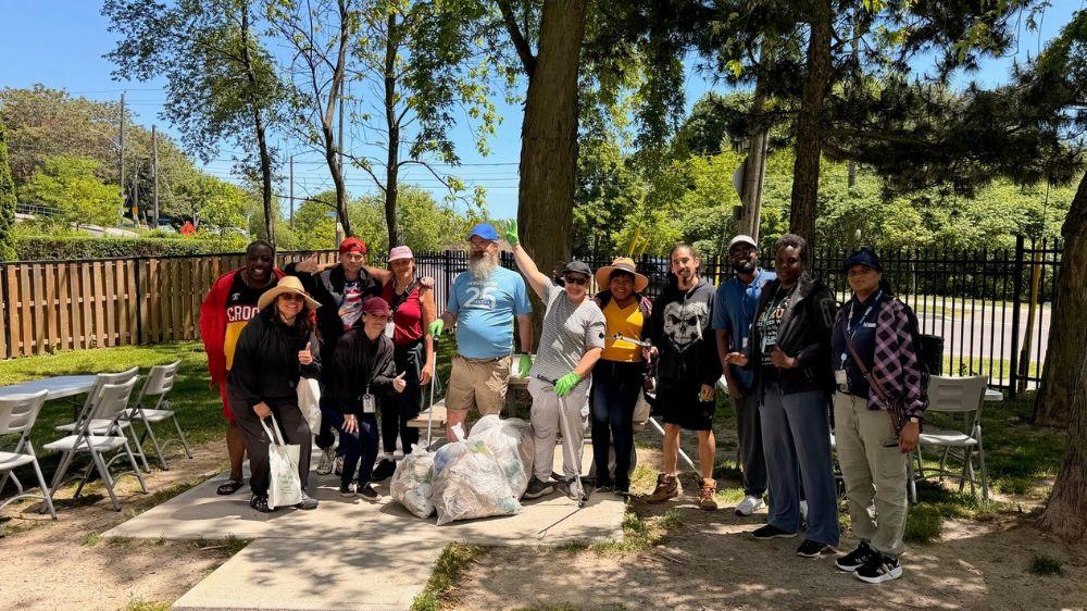 A group of people posing for a photo. They are holding garbage bags and litter grabbers