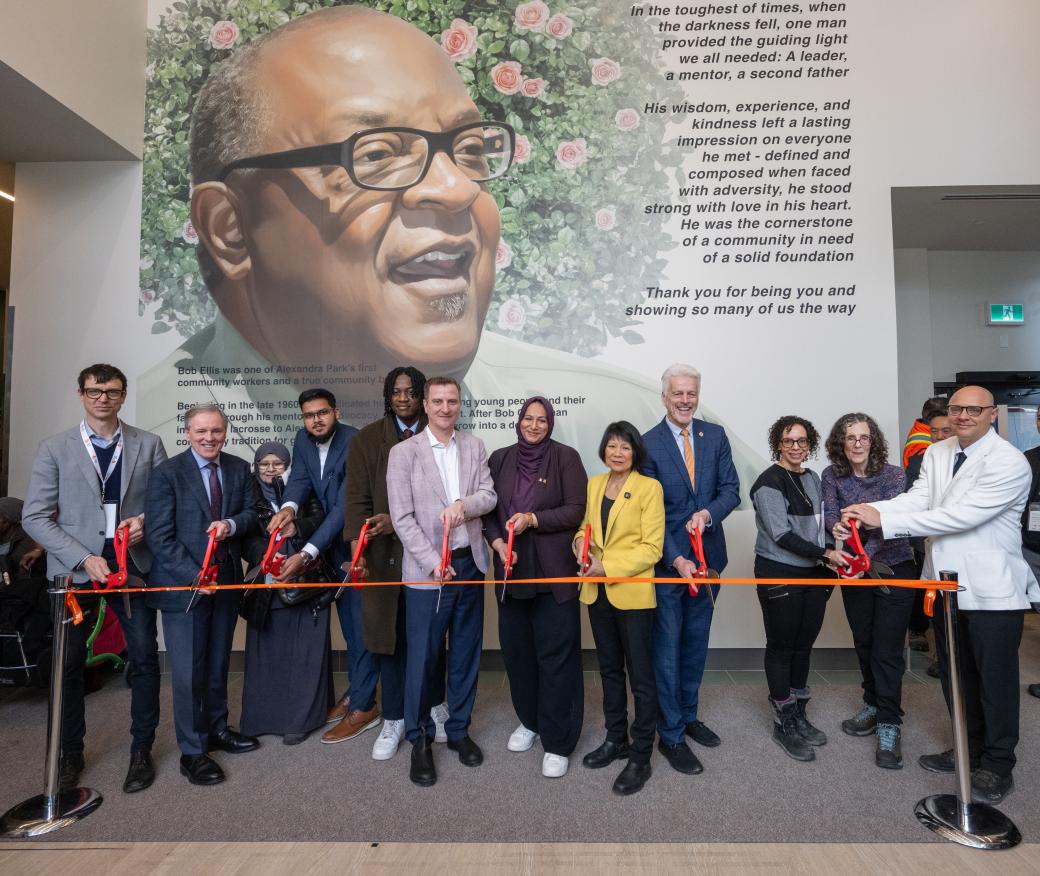 Group of people cutting a ceremonial ribbon in front of a mural