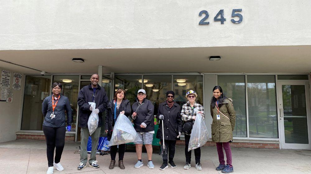 A group of people standing in front of a building and posing for a photo while holding garbage bags and litter grabbers.