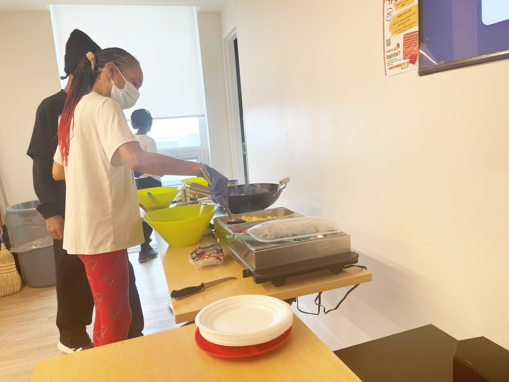 A woman cooking breakfast with a frying pan in a community room.