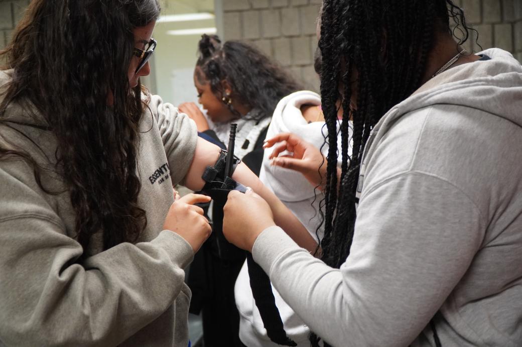 Three women in a community centre learning first aid. One woman has a tourniquet around her arm.