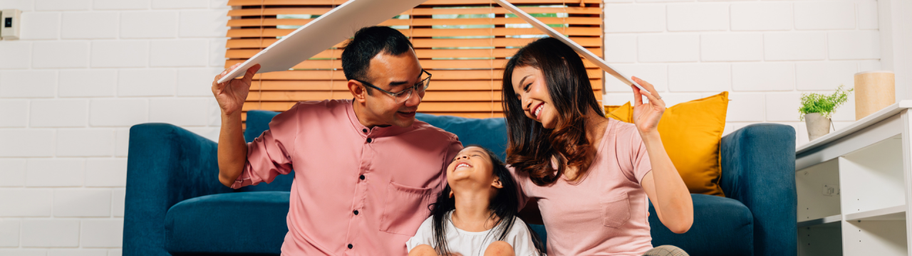 A family sitting next to a couch playing with a cardboard roof over their heads
