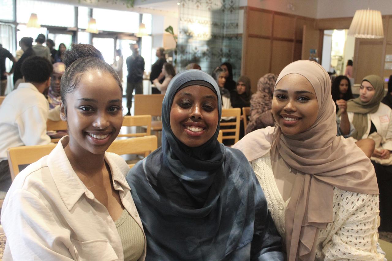 Three ladies sitting and smiling for the camera at an event. 