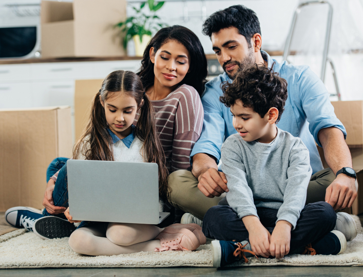Two adults and two children sitting on the floor looking at a laptop