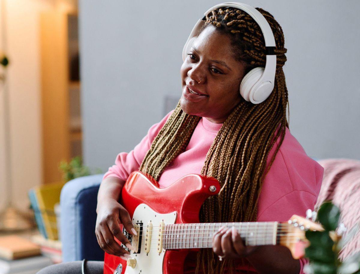 A woman who is wearing a pink sweater is playing a red bass guitar. 