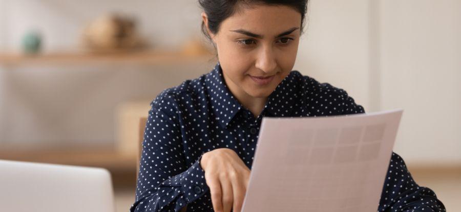 A woman who is wearing a blue and white polka dots shirt is reading notes from a sheet of paper.