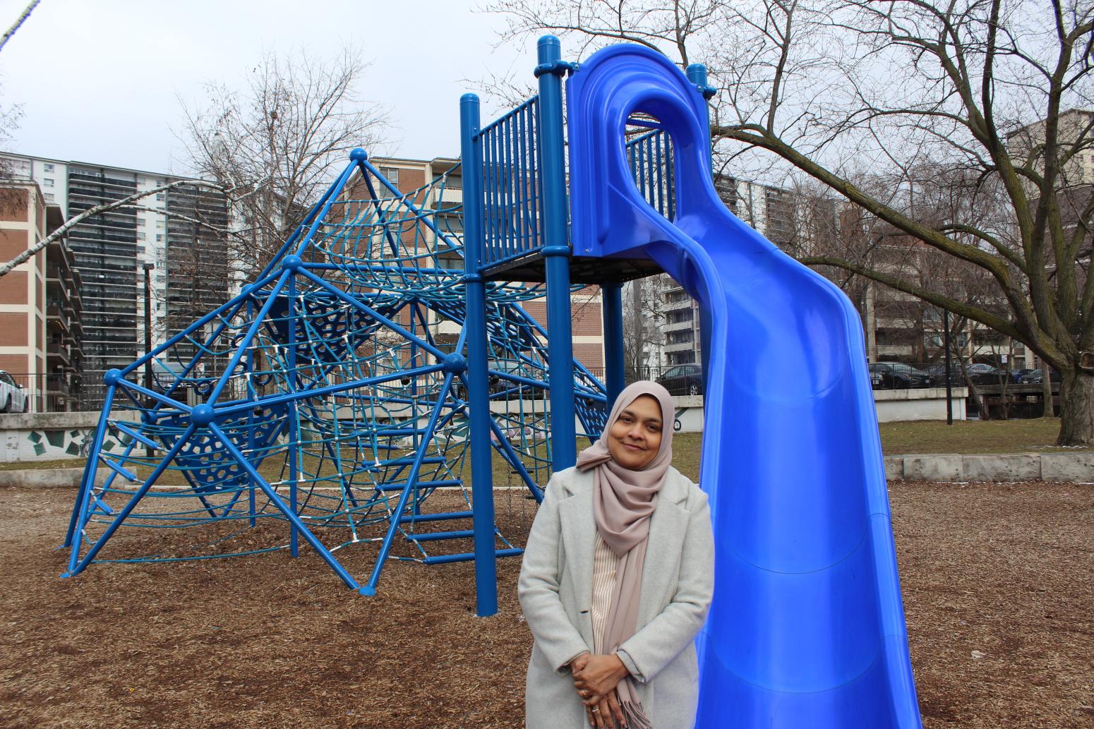 A person is standing besides a blue playground slide