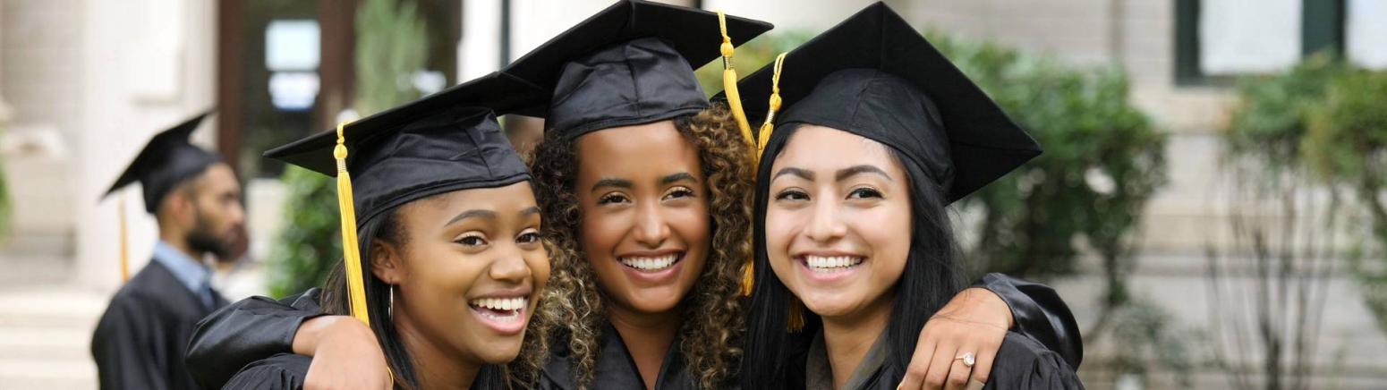 Three young women wearing graduation caps and smiling.