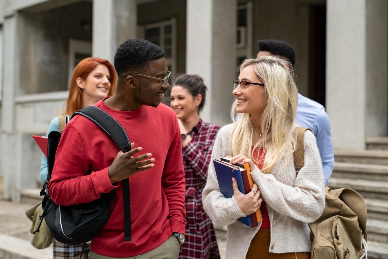 Two students holding books and talking to each other