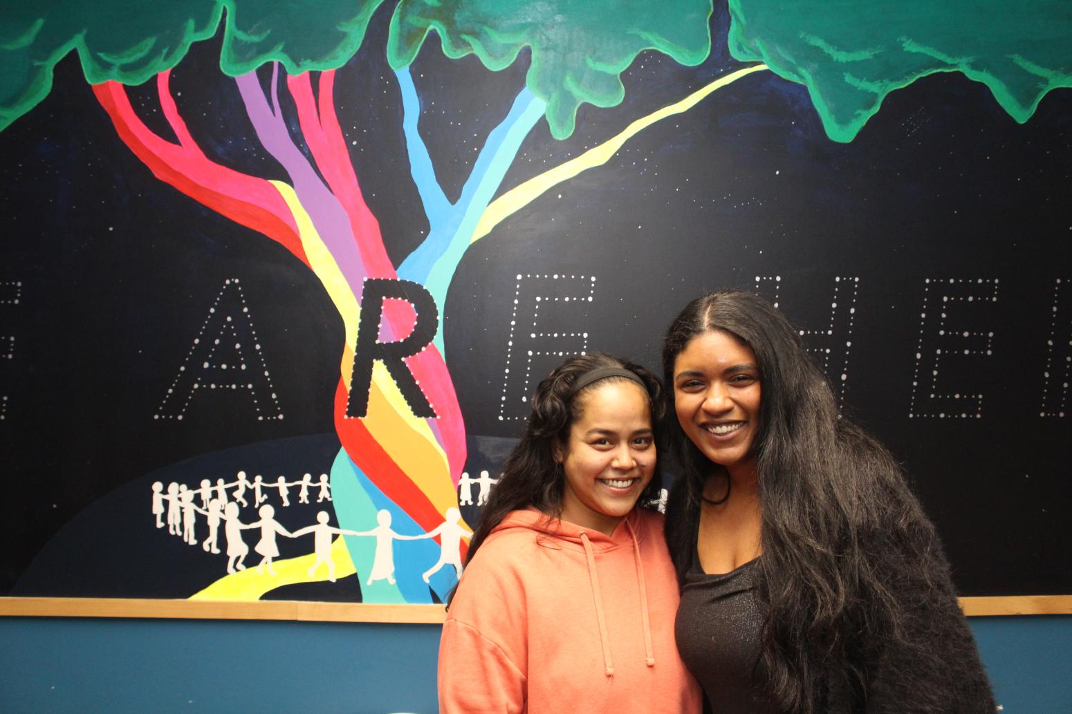 Two Homeward Bound participants posing in front of a mural of a multi-coloured tree with a black background