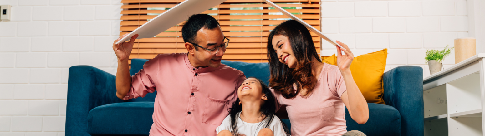 A family sitting next to a couch playing with a cardboard roof over their heads