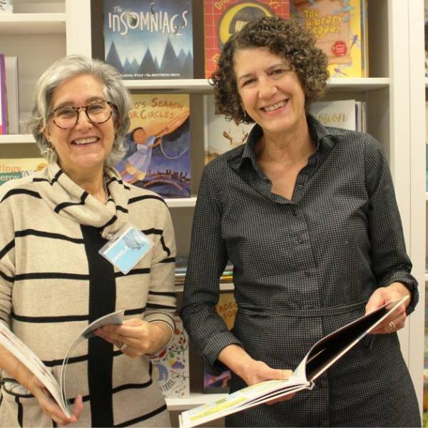 A staff member from The Children's Book Bank alongside Executive Director, Mary Ladky, in front of a book shelf.