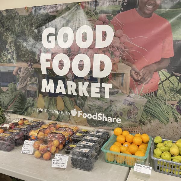 A table with a variety of fruits. A Good Food Market poster is on the wall. 
