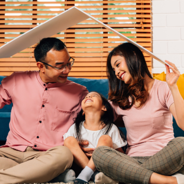 A family sitting next to a couch playing with a cardboard roof over their heads