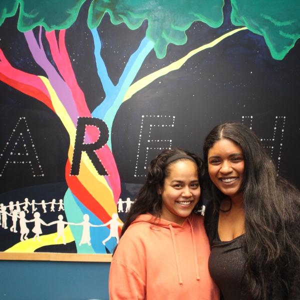 Two Homeward Bound participants posing in front of a mural of a multi-coloured tree with a black background