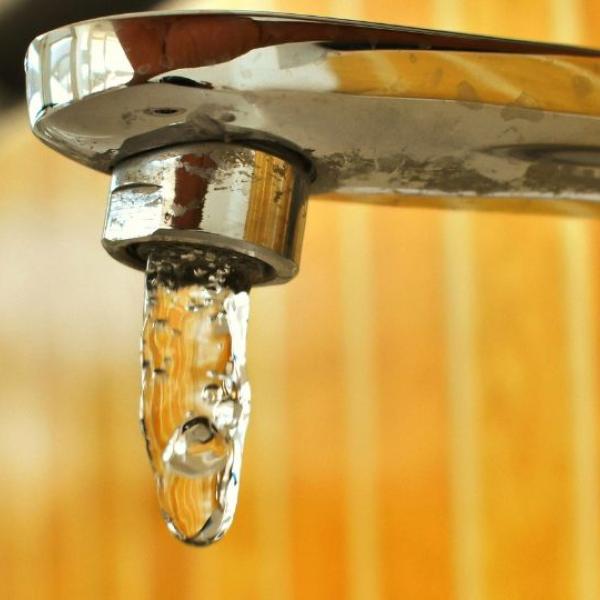 A close-up of a chrome faucet with water dripping from the spout against a blurred background of wooden paneling.